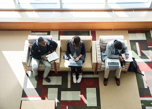 Three students sit in the library studying